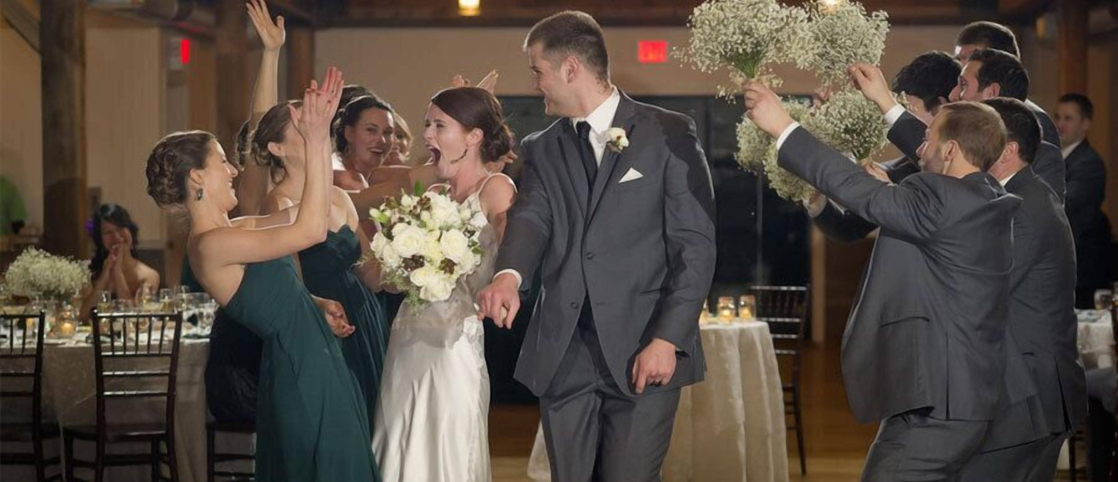 A wedding reception with guests clapping and holding bouquets.
