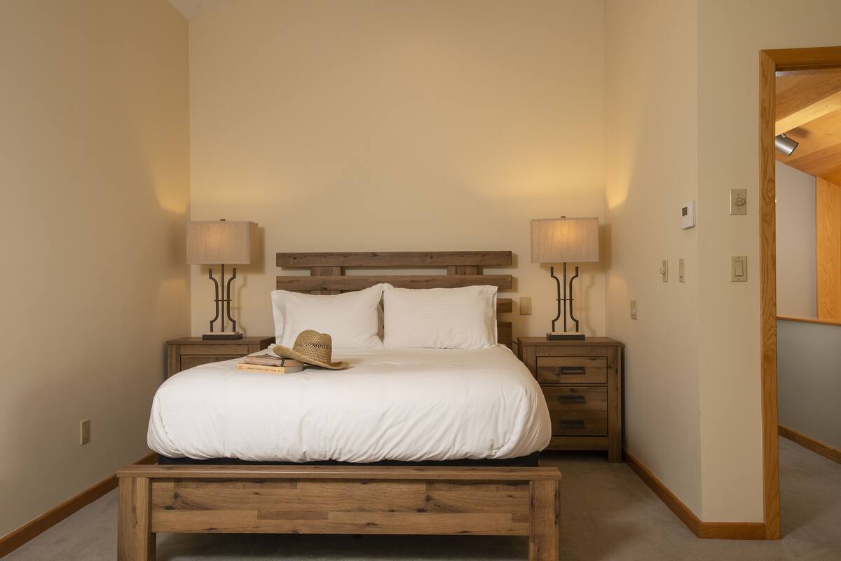 Un dormitorio con una cama de madera, dos mesitas de noche con lámparas, una mesita auxiliar y un espejo.
