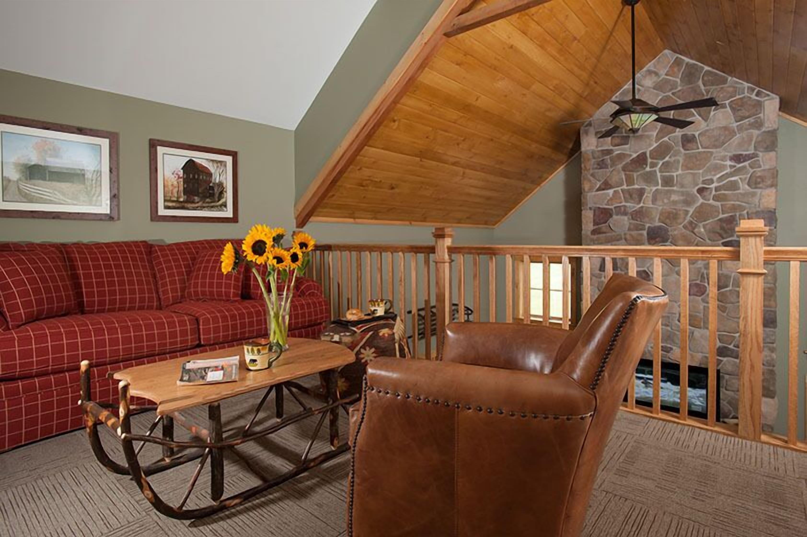A cozy living room with a red sofa, a brown leather chair, a wooden coffee table, and a stone fireplace.