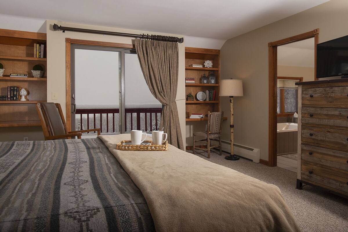 Un dormitorio acogedor con una cama grande, un aparador de madera, un escritorio con silla y una estantería.