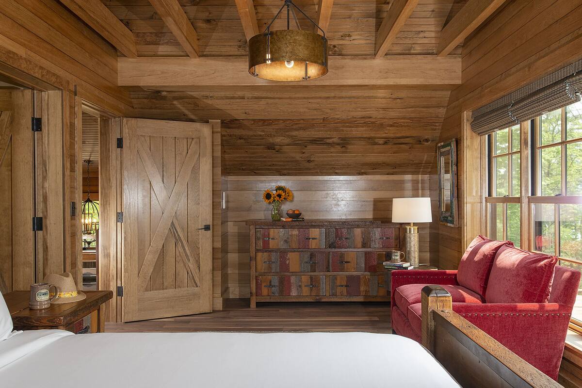 Interior rústico de una cabaña con una cama, un sofá rojo, un armario de madera y una lámpara colgante.