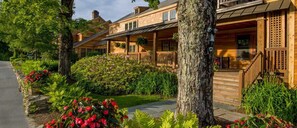 A wooden cabin-style building with a porch, surrounded by lush greenery and flowering plants. - The Mountain Top Inn & Resort (Chittenden)