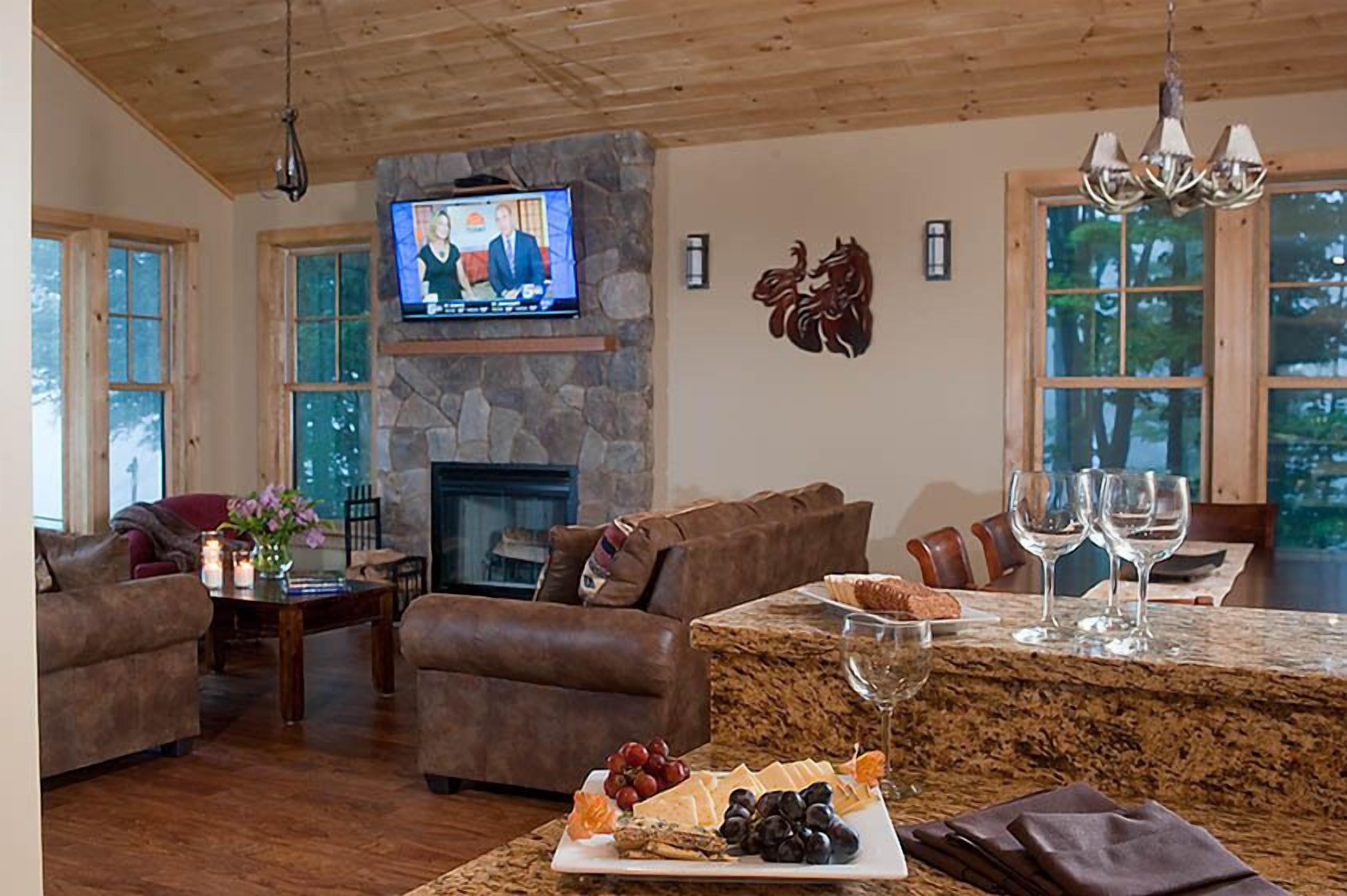 A cozy living room with a stone fireplace, a television mounted above it, and a dining area with a marble table set for two.
