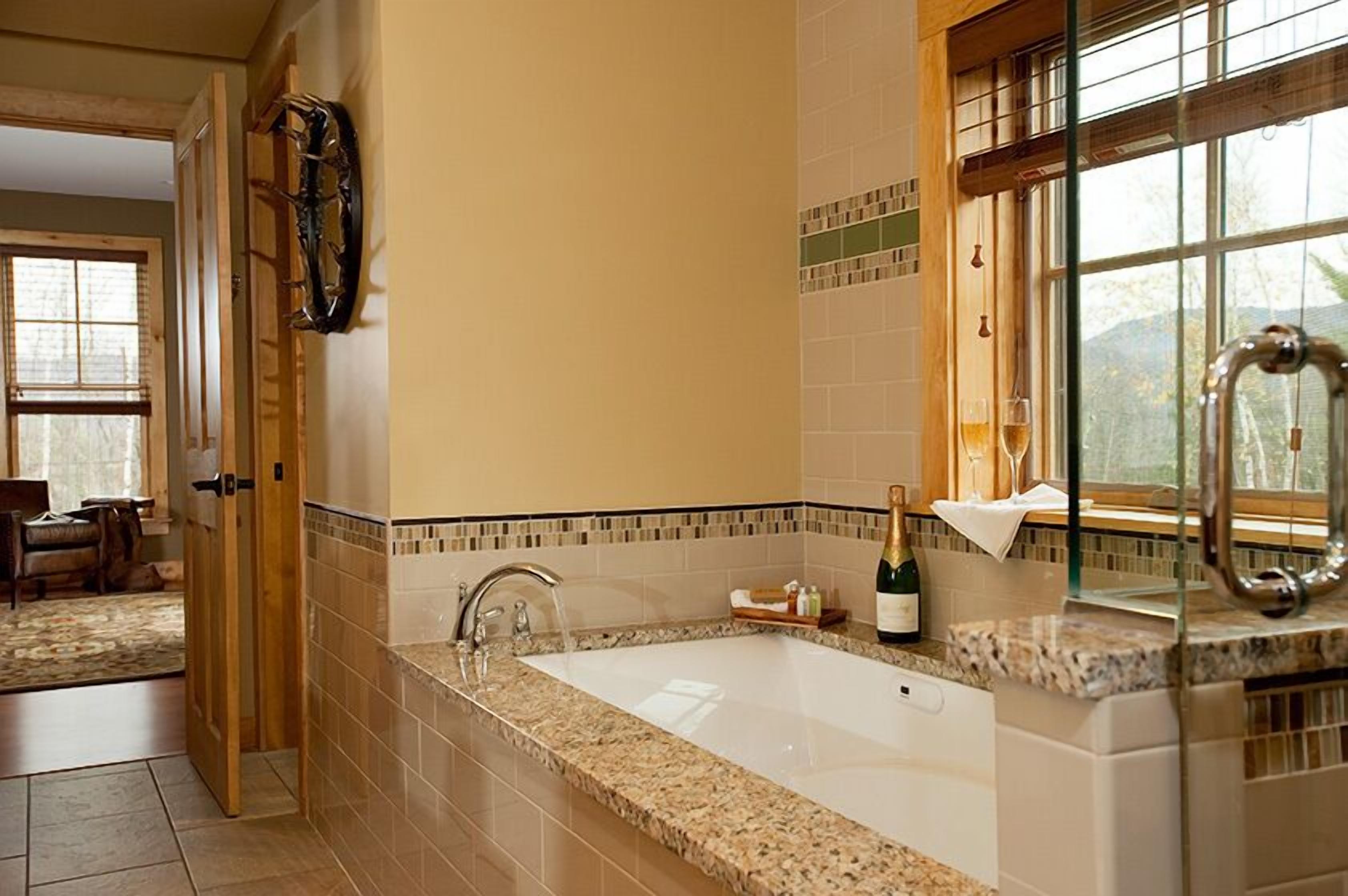 A bathroom with a large bathtub, a wine bottle on the counter, and a window with a view.