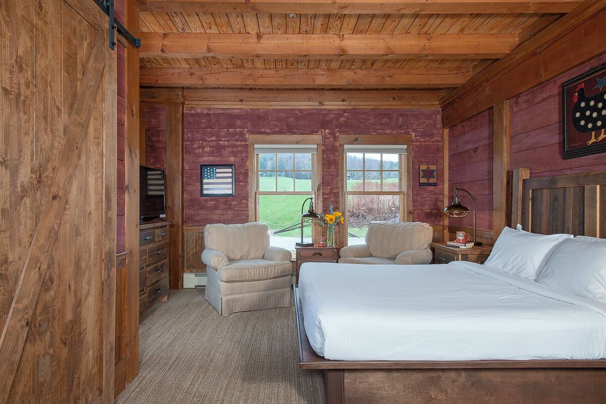 Un dormitorio de cabaña de madera con una cama, dos sillones, un tocador y un televisor.