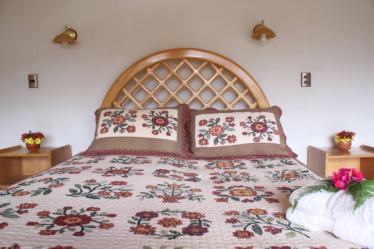 Una cama con cabecera de madera, ropa de cama floral y dos mesitas de noche con lámparas.