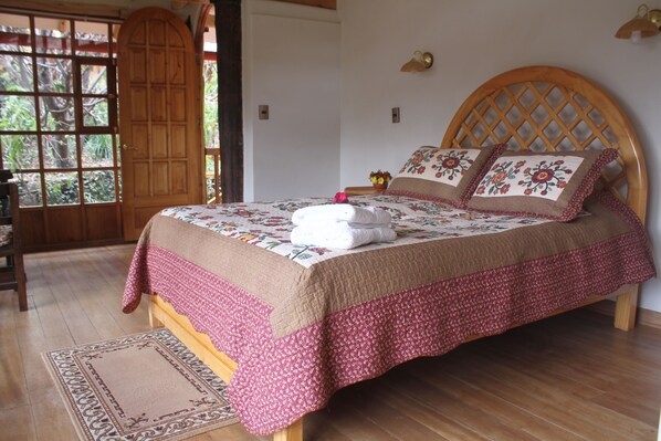Un dormitorio con cama de madera, ropa de cama floral y vistas a través de una gran puerta de madera.