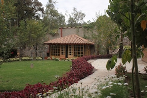 Un bâtiment traditionnel, doté d’un toit en tuiles et de grandes fenêtres, entouré d’un jardin bien entretenu et accessible par un chemin.