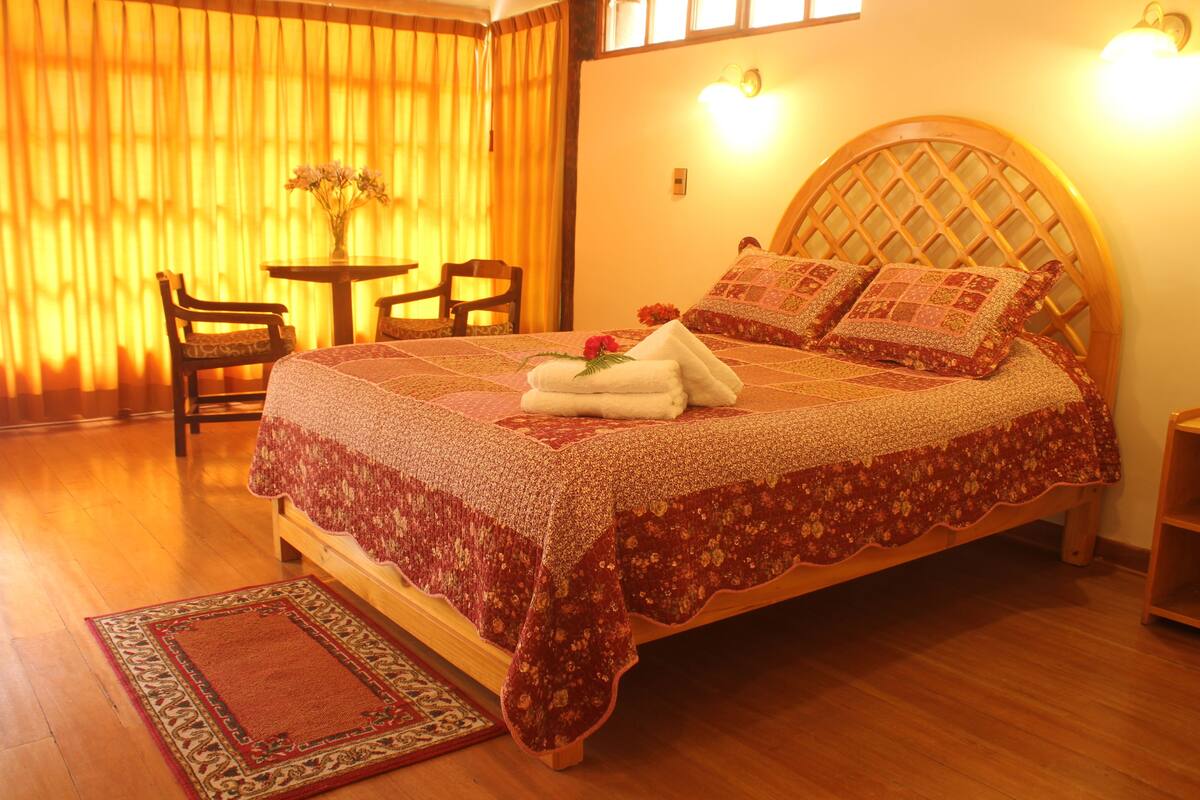 Una cama bien hecha con una colcha floral, un cabecero de madera y una mesita de noche con un florero.