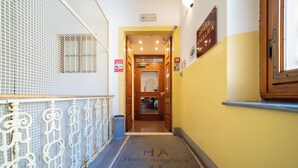 A hotel hallway with a metal railing, a door leading to a room, and a sign indicating room rates. - Hotel Angelica (Florence)
