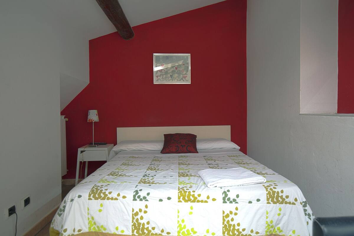 A bedroom with a bed, a nightstand, a lamp, and a painting on the wall.