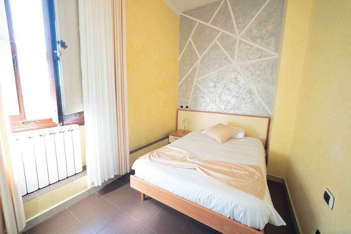 A hotel room with a wooden bed, a nightstand, a wall-mounted light, and a radiator.