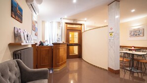 A hotel lobby with a reception desk, a waiting area with a sofa, and a dining area with tables and chairs. - Hotel Angelica (Florence)