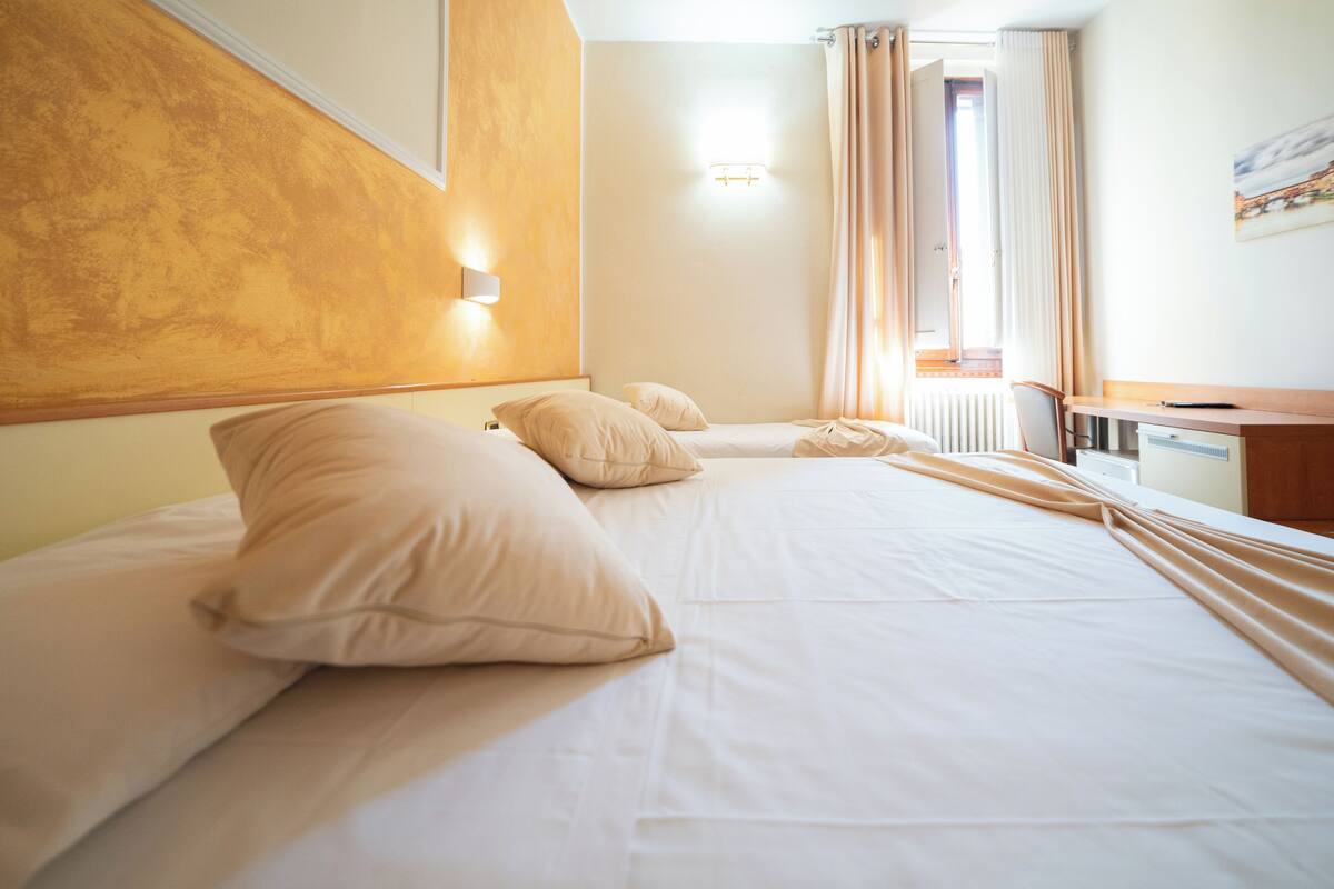 A hotel room with two beds, a desk, and a window with curtains.