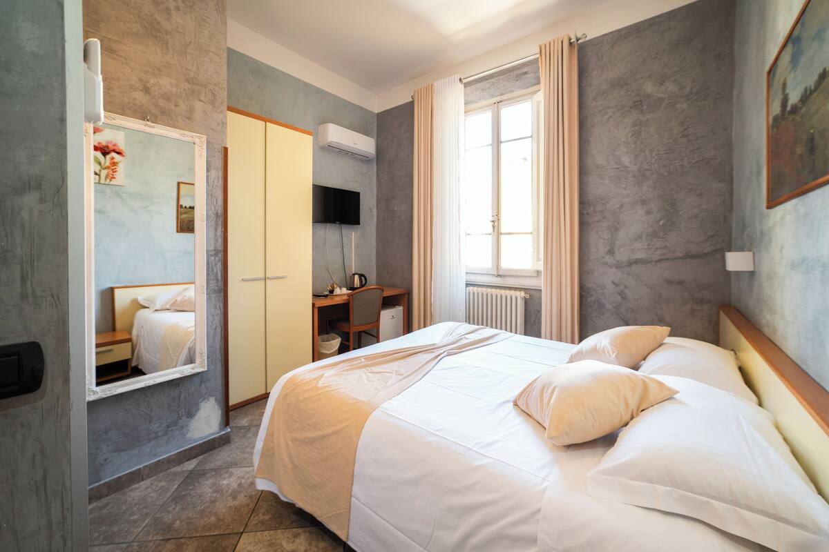 A hotel room with a bed, a desk, a chair, a TV, and a window with curtains.