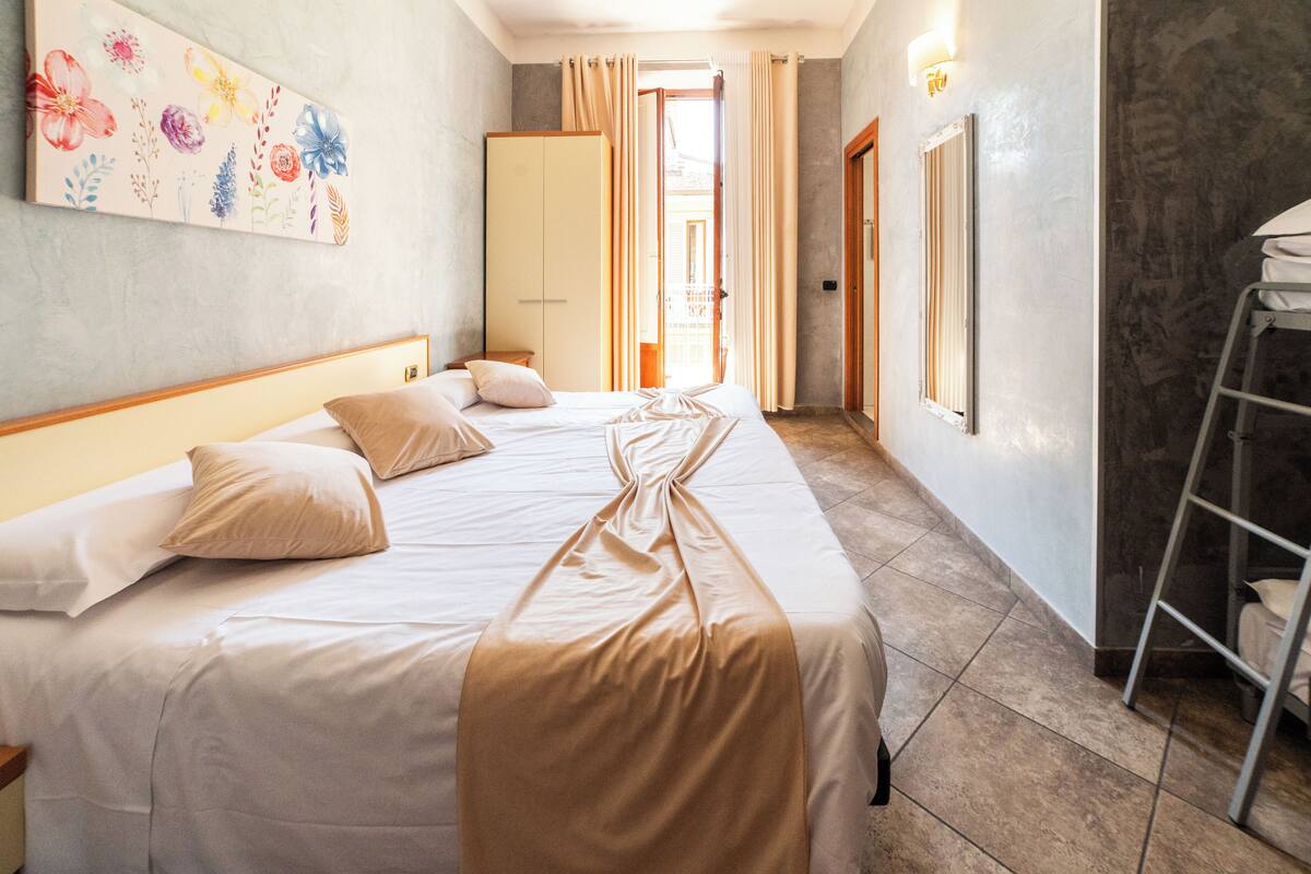 A hotel room with a large bed, a wardrobe, a ladder, and a painting on the wall.