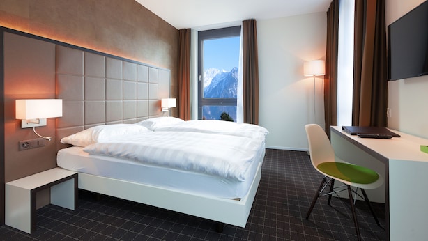 Habitación de hotel moderna con cama, escritorio, silla y vistas a las montañas a través de una ventana.