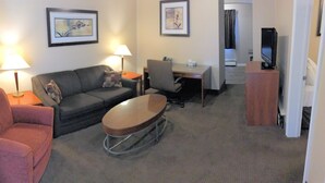A hotel room with a sofa, a small table, a desk, a chair, a television, and framed artwork on the walls. - The Lincoln Inn (North Bay)