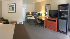 A hotel room with a bed, a desk, a chair, a television, and a bathroom with a sink and mirror. - The Lincoln Inn (North Bay)