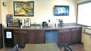 A kitchen area with a granite countertop, a coffee maker, a sink, and a television mounted on the wall. - The Lincoln Inn (North Bay)