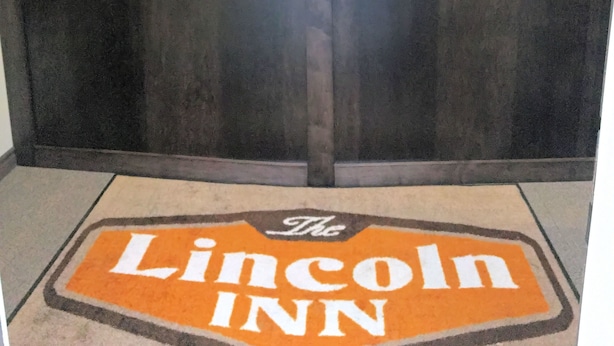 A reception desk with a clock, a welcome sign, and a framed picture on the wall. - The Lincoln Inn (North Bay)