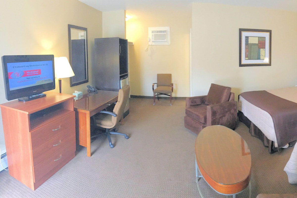 Habitación de hotel con escritorio, dos camas, una silla, televisión y un cuadro en la pared.