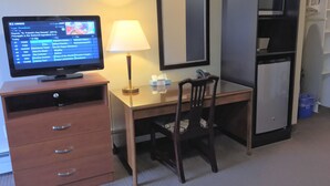 A hotel room with a desk, chair, television, lamp, and a minibar. - The Lincoln Inn (North Bay)