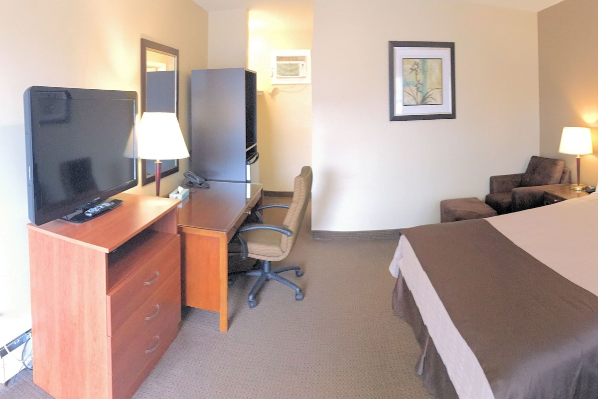 Una habitación de hotel con una cama, dos mesitas de noche con lámparas, un escritorio con una silla, un televisor y un armario.