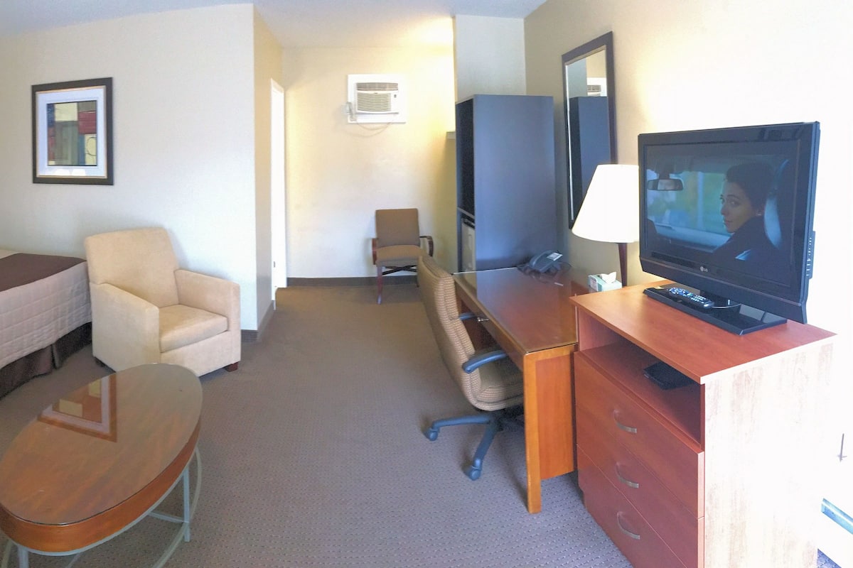 Habitación de hotel con dos camas, un escritorio con televisor, una silla y una mesita.