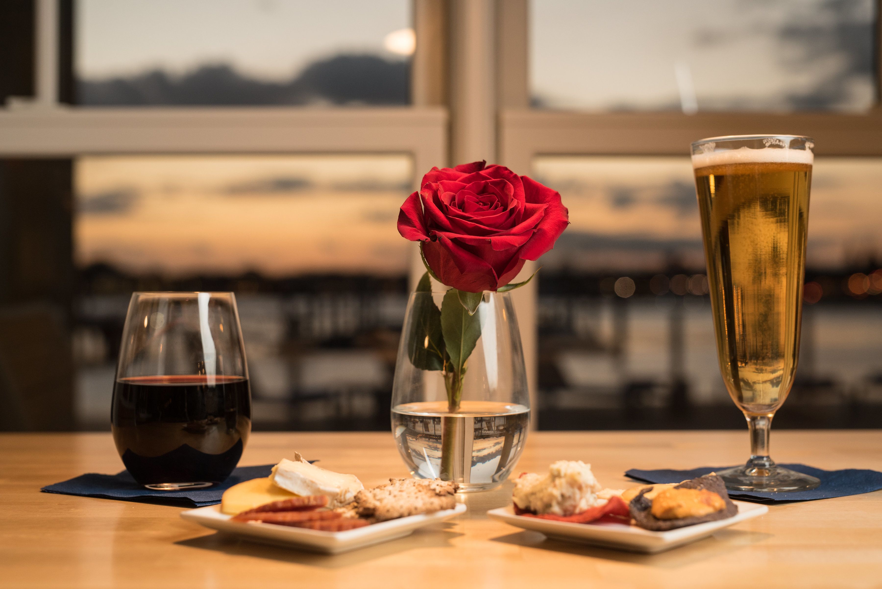 Ein Tisch mit einem Weinglas, einem Bierglas, einer Rose in einer Vase und kleinen Teller mit Speisen.