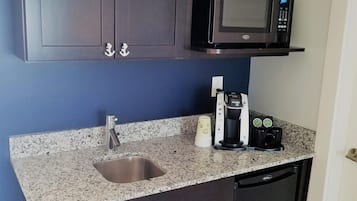 Cocina compacta con armarios oscuros, microondas, lavamanos y cafetera.