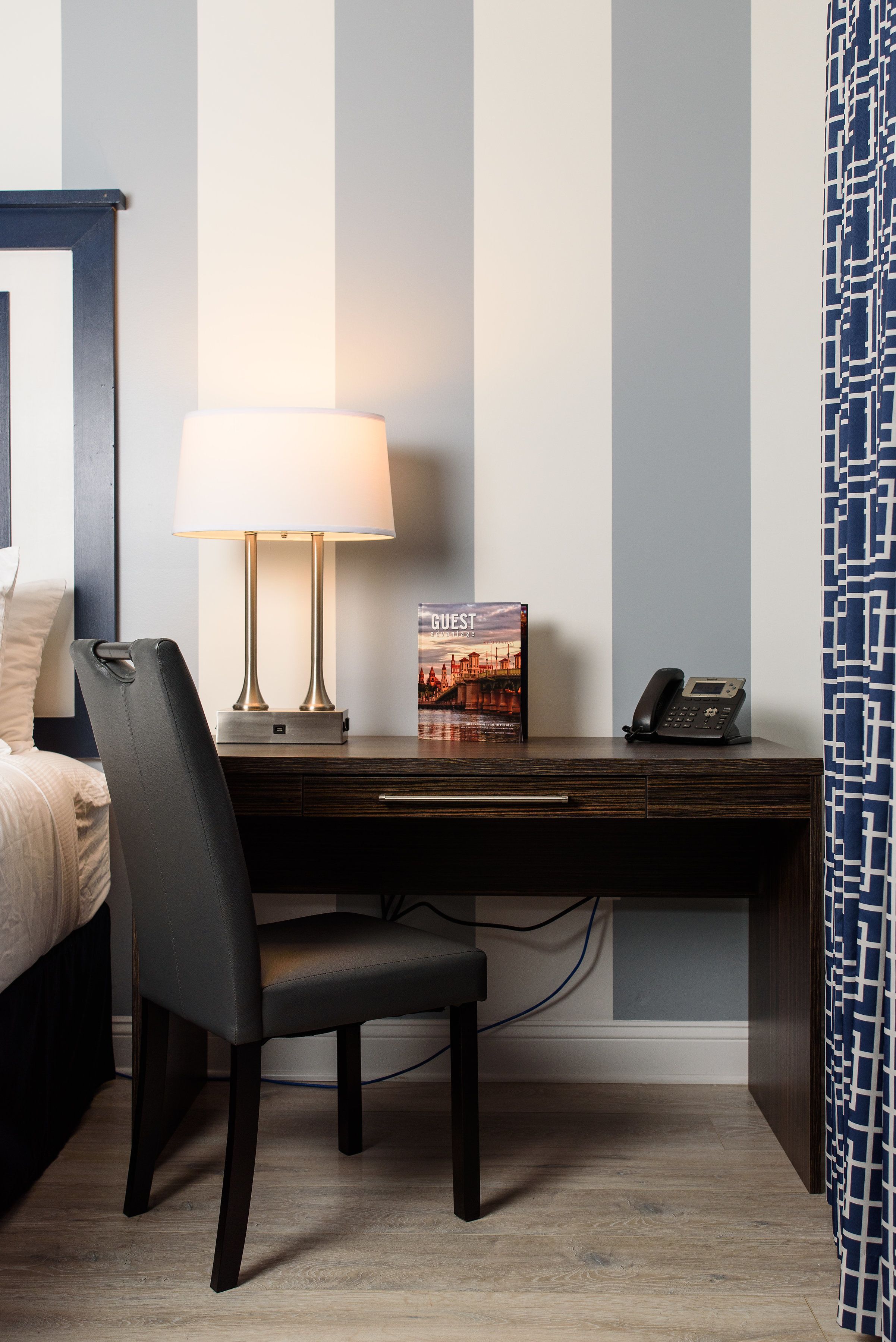 Ein Hotelzimmer mit Bett, Schreibtisch mit Lampe, Telefon und einem gerahmten Bild an der Wand.
