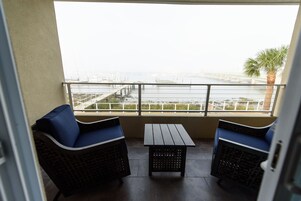 A balcony with two wicker chairs, a small table, and a view of a bridge over water.