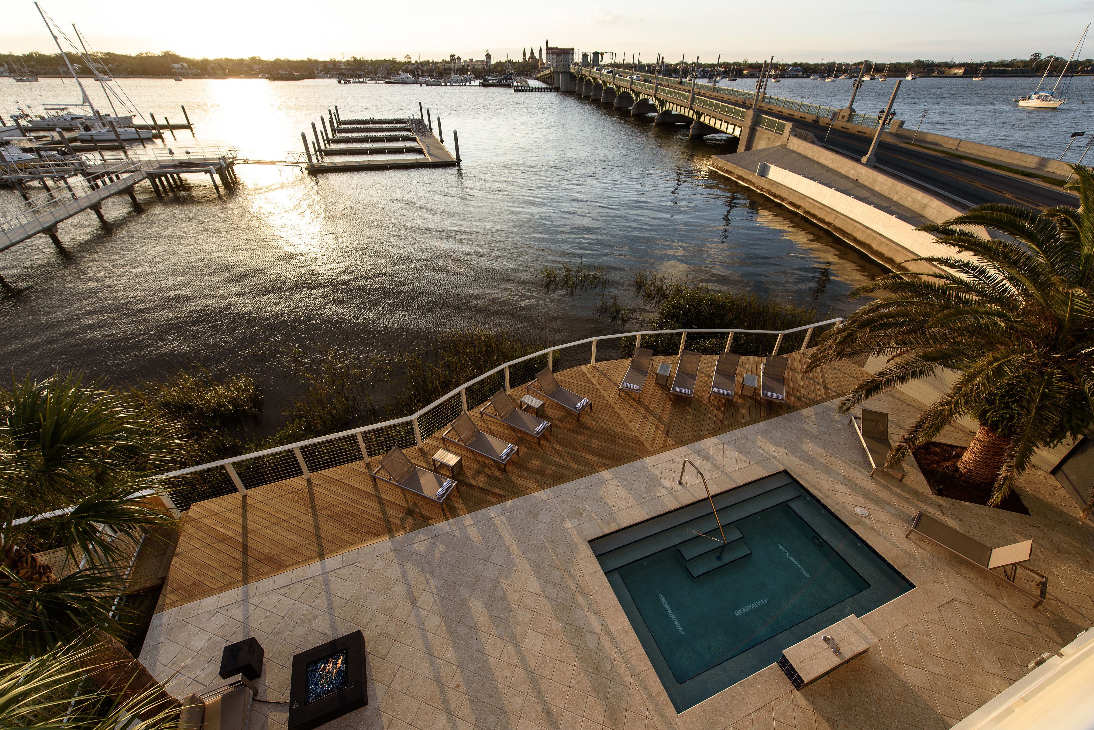 Un espace piscine doté de chaises longues et d’une petite piscine, offrant une vue sur une marina avec des bateaux et un pont.