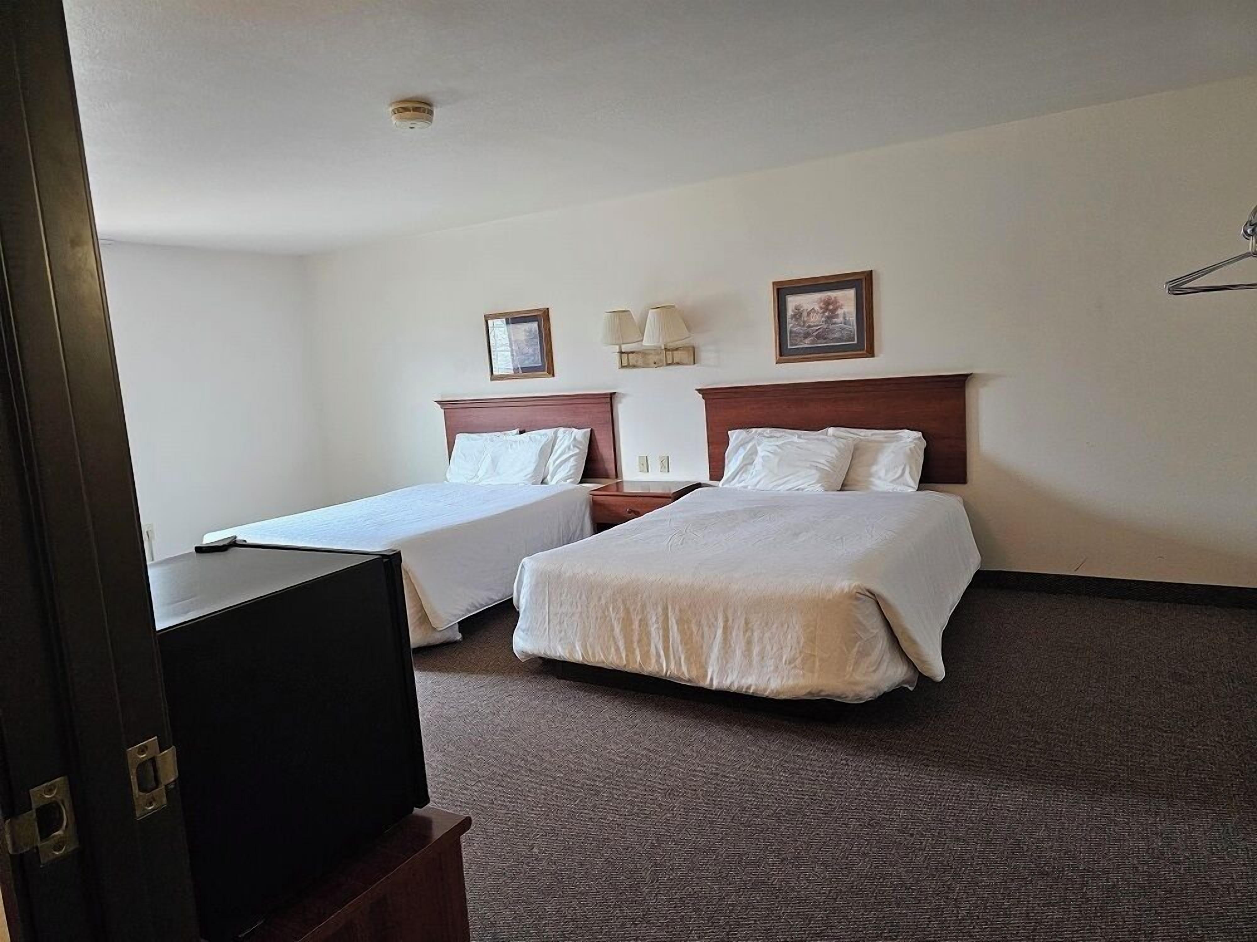 A hotel room with two beds, a desk, a television, and a lamp.