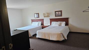 A hotel room with two beds, a desk, a television, and a lamp.