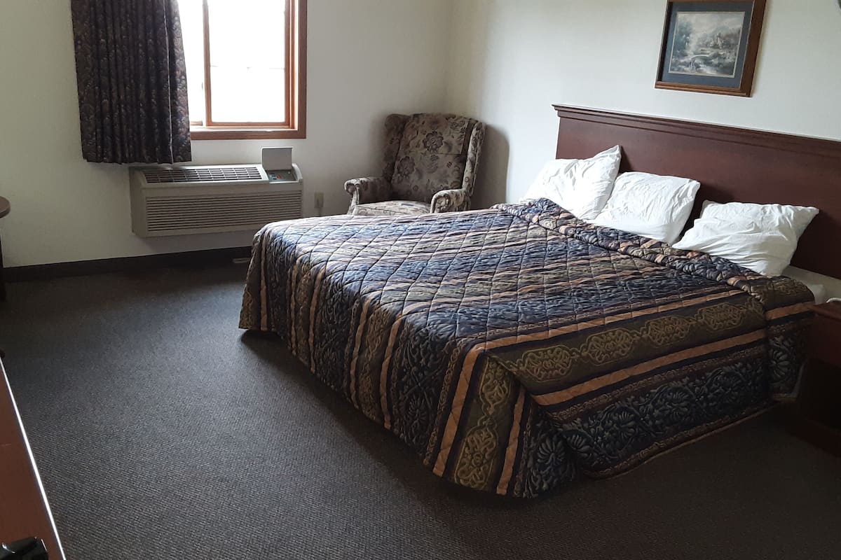 A hotel room with a bed, a chair, a desk, and a window.