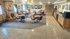 A dining area with multiple tables and chairs, a fireplace, and a kitchen area with a refrigerator and sink. - Park View Inn & Suites and Conference Center (West Bend)