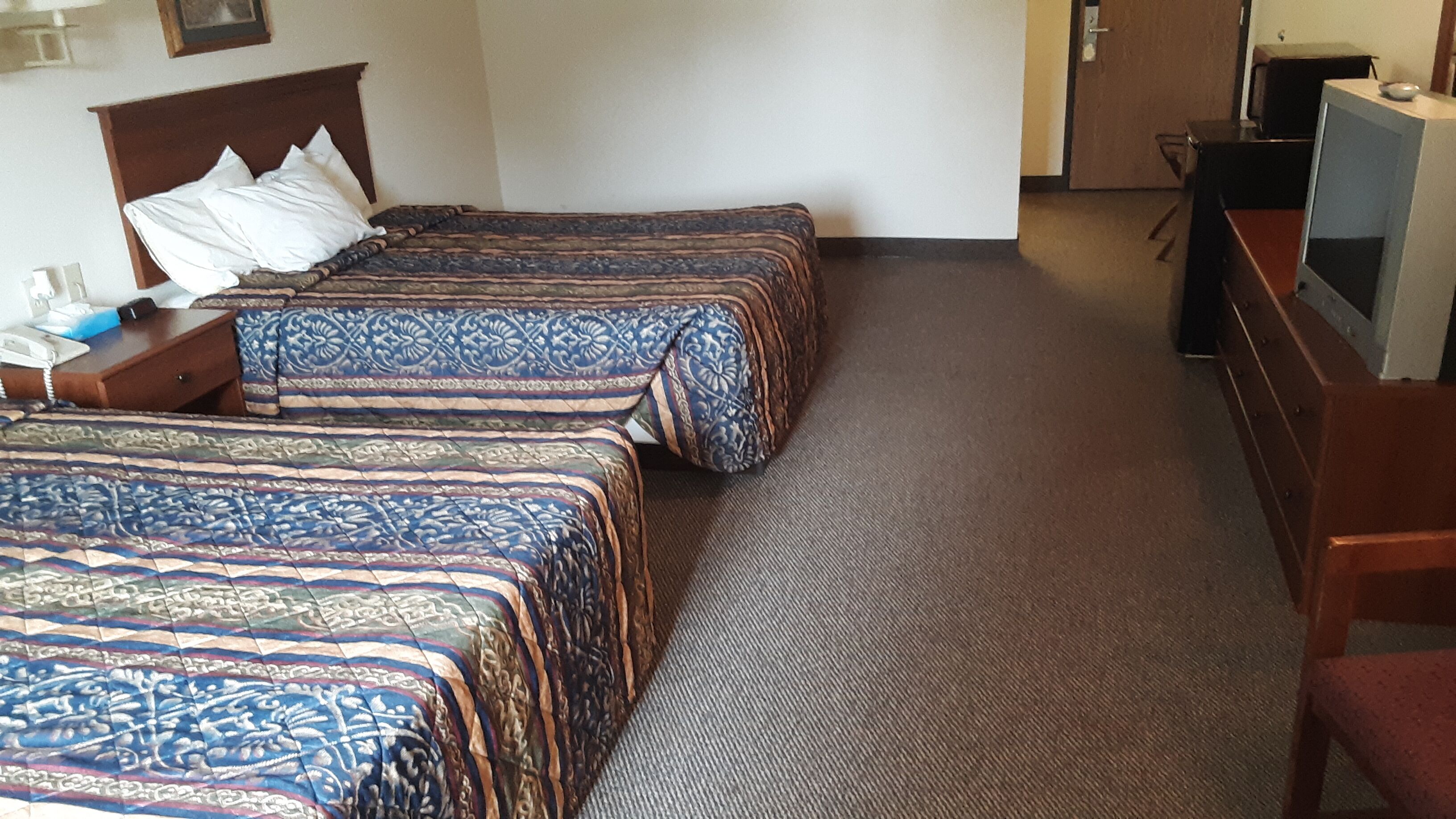 A hotel room with two beds, a desk with a telephone, and a television.