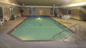 An indoor swimming pool with a tiled floor, a pool ladder, and a seating area with tables and chairs around the pool. - Park View Inn & Suites and Conference Center (West Bend)
