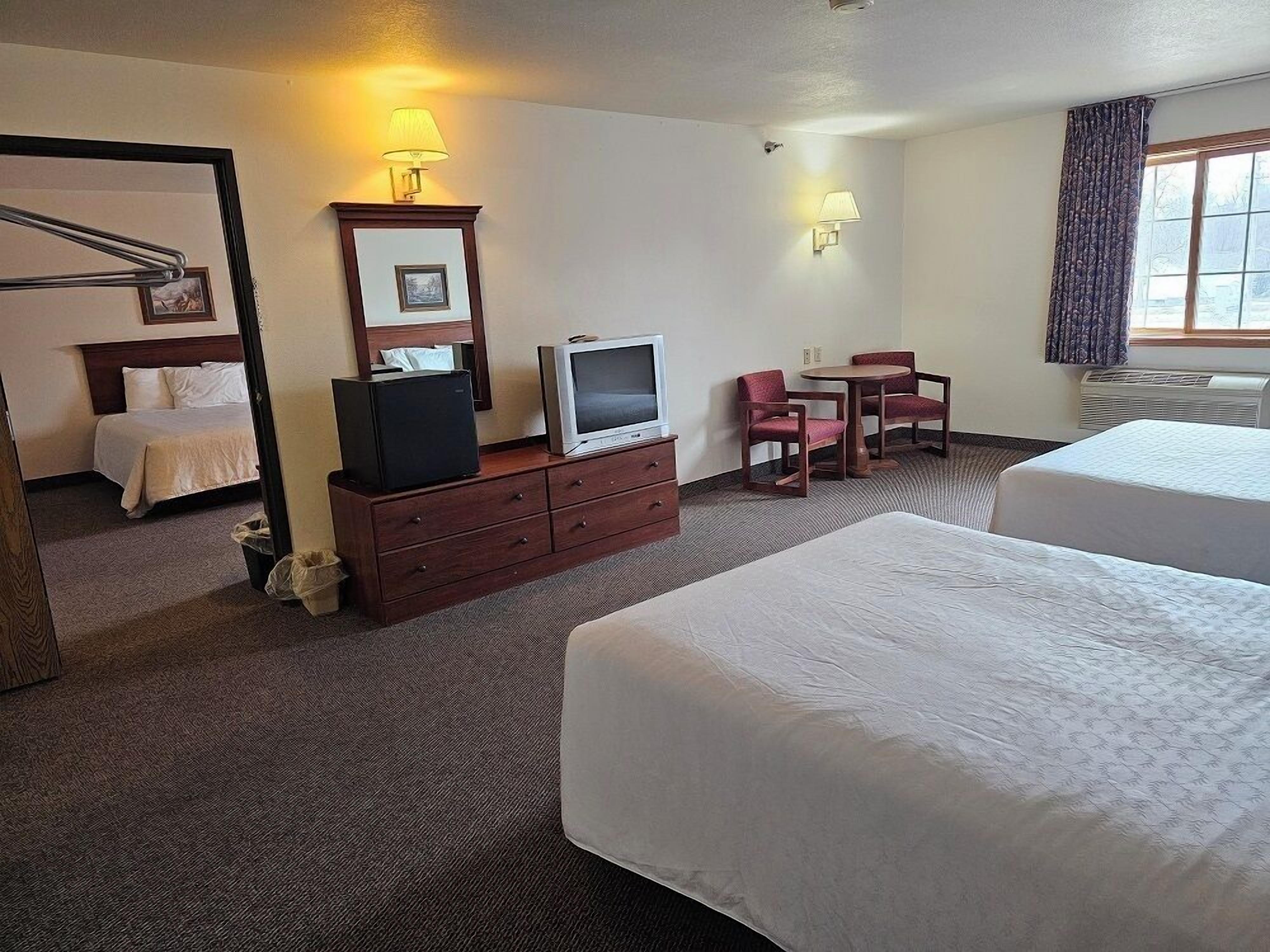 A hotel room with two beds, a TV on a dresser, a desk with a chair, and a window with curtains.