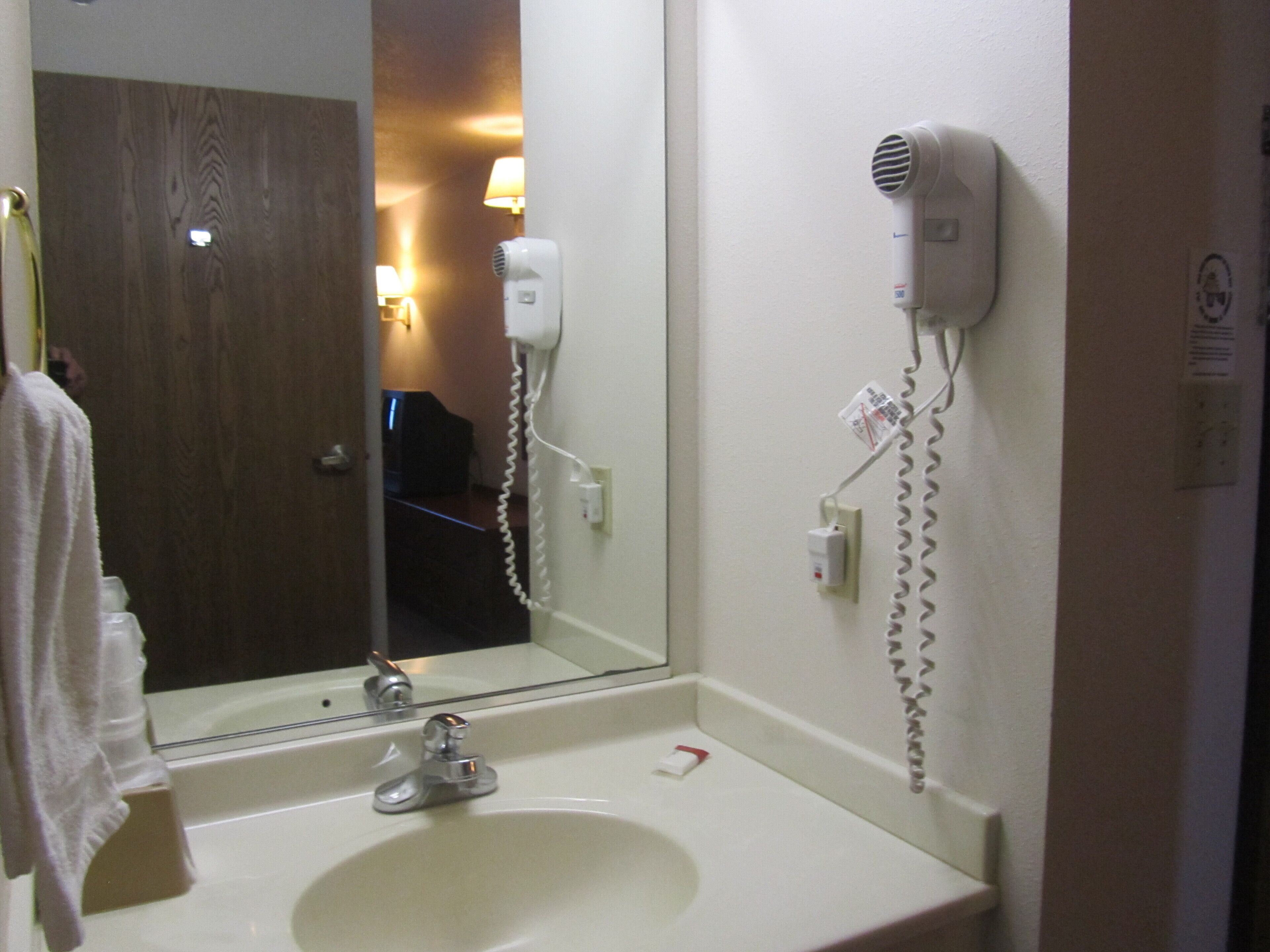 Un baño con lavamanos, espejo y secador de pelo montado en la pared.