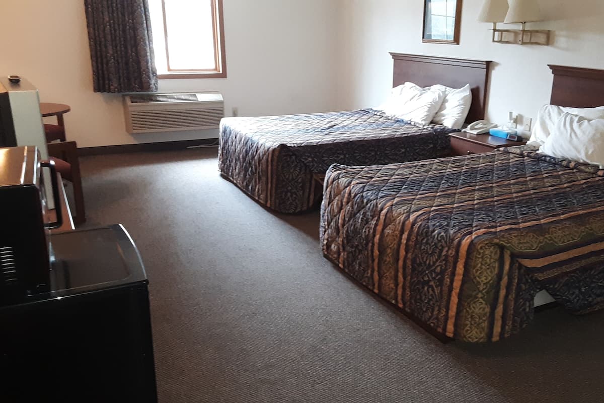 A hotel room with two beds, a desk, a chair, a TV, and a window with curtains.