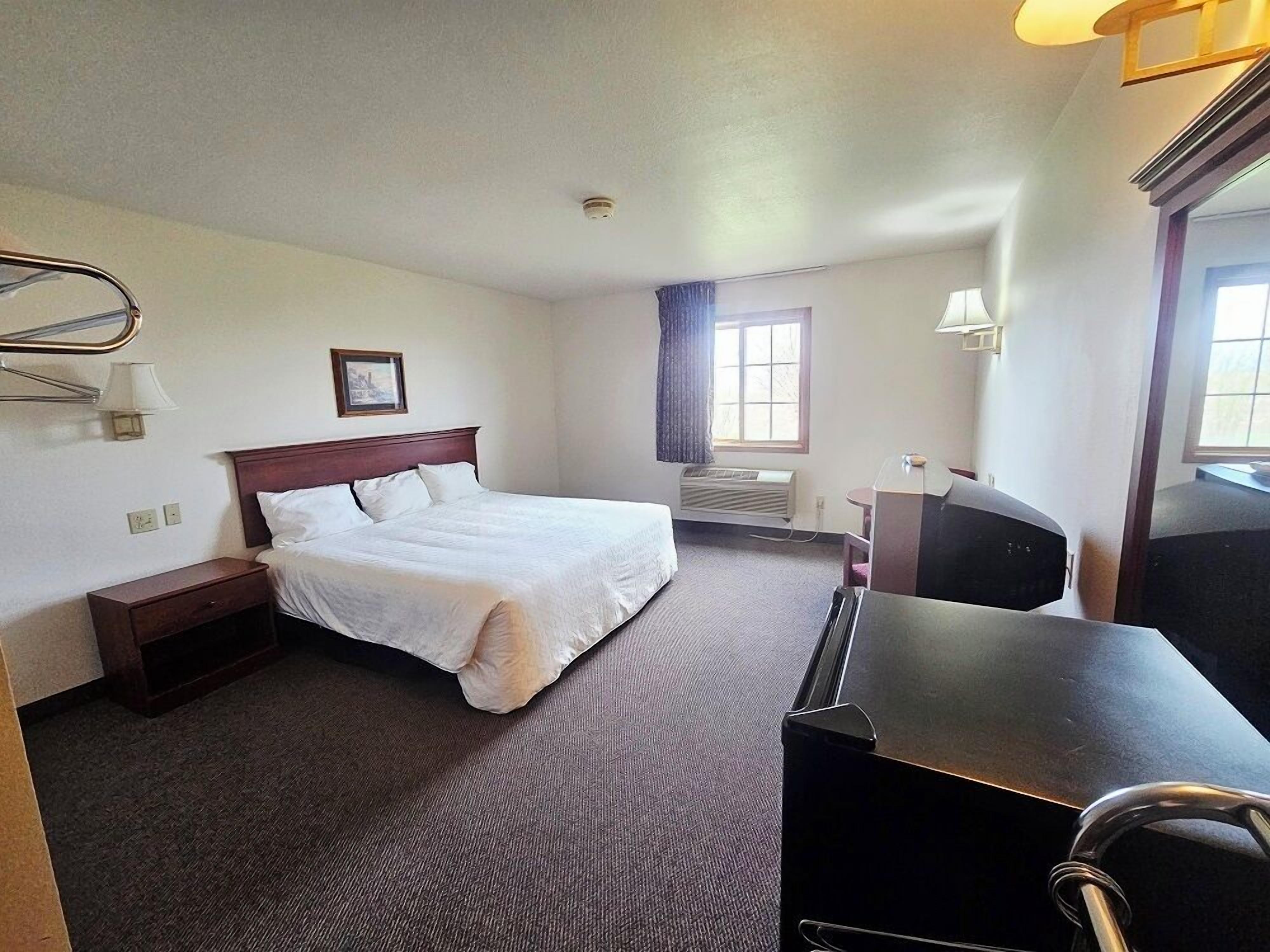 A hotel room with a bed, bedside table, desk, chair, and a window with curtains.