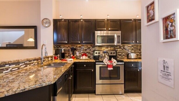 A modern kitchen with dark cabinets, stainless steel appliances, and a granite countertop. - Encantada Resort by Home 2U (Kissimmee)
