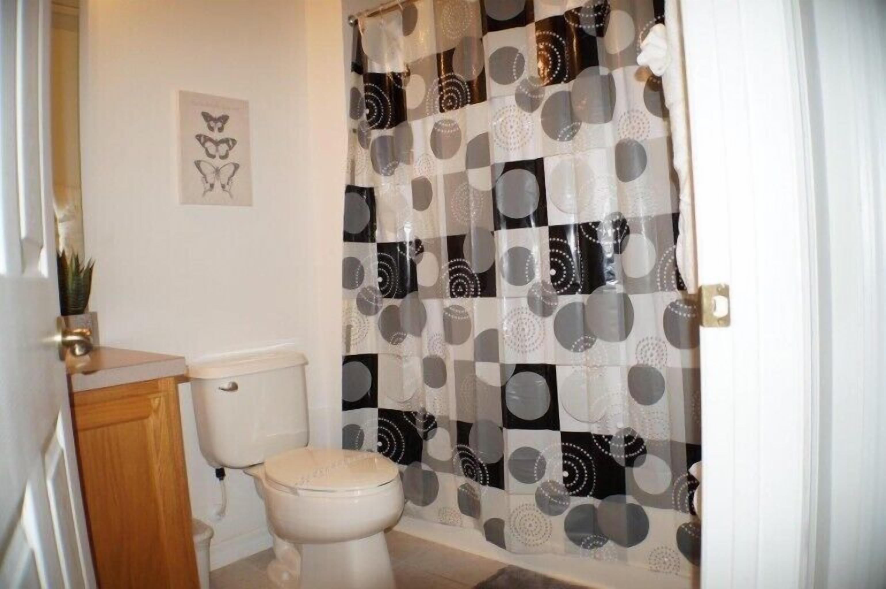 Un baño con inodoro, lavamanos y cortina de ducha estampada con un diseño geométrico.