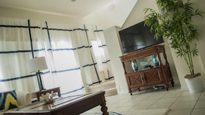A living room with a TV, a wooden cabinet, a dining table, and a large plant. - Encantada Resort by Home 2U (Kissimmee)