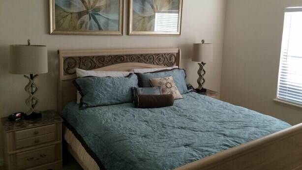 Een slaapkamer met een bed, twee nachtkastjes, twee wandlampen en twee ingelijste kunstwerken boven het bed.