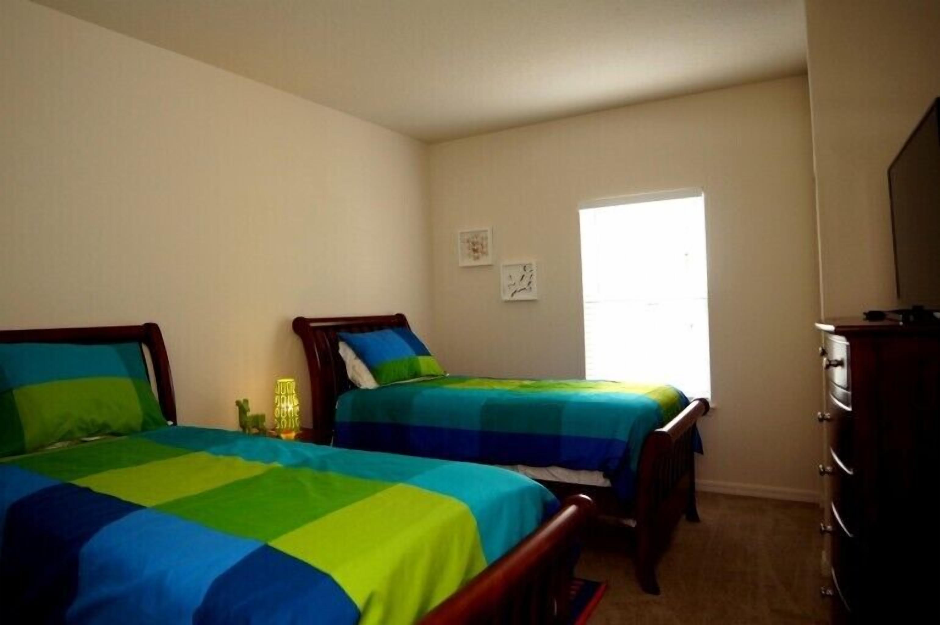 A bedroom with two beds, a dresser, and a window.
