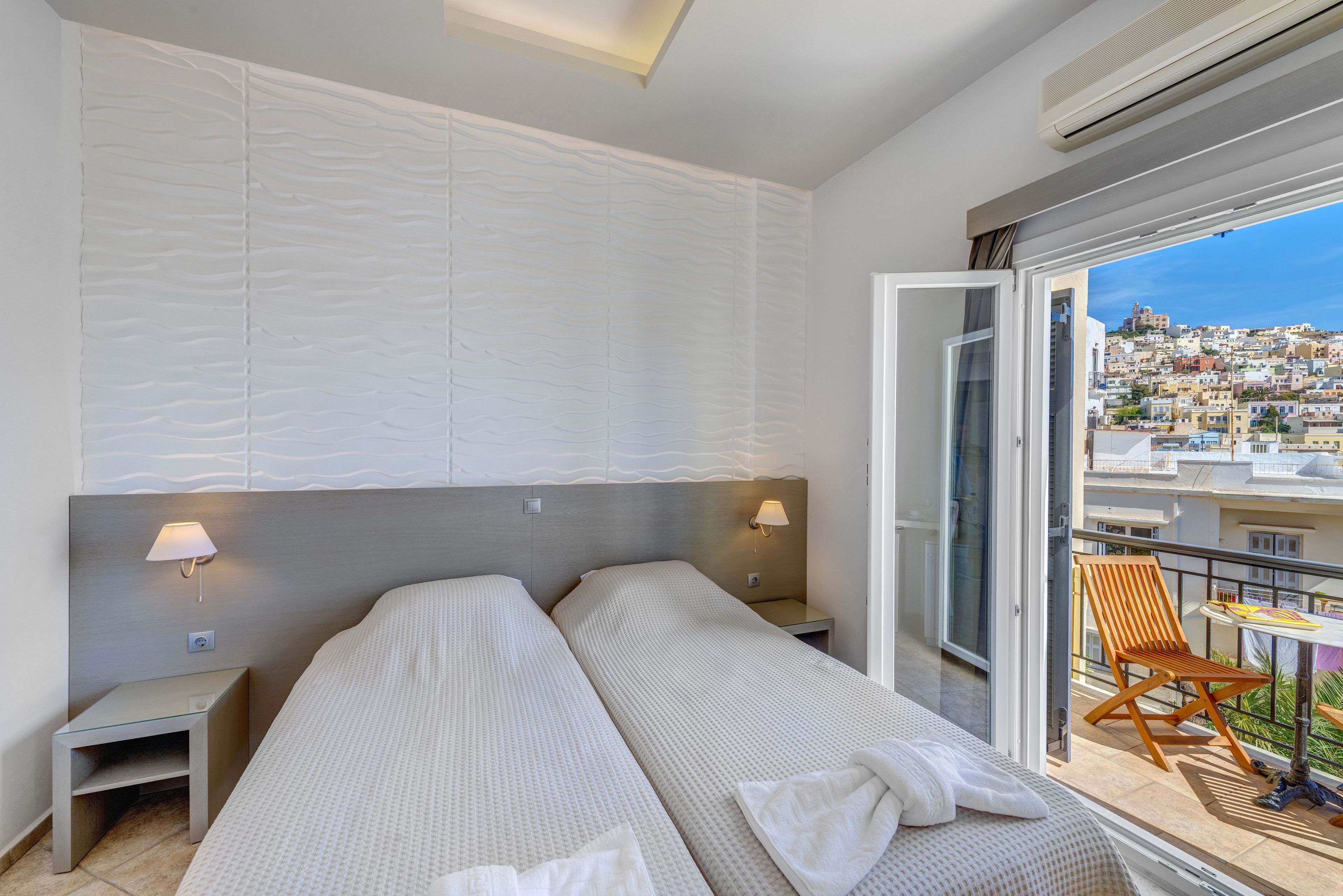 Une chambre d’hôtel avec deux lits, un balcon avec une chaise et une vue sur la ville.